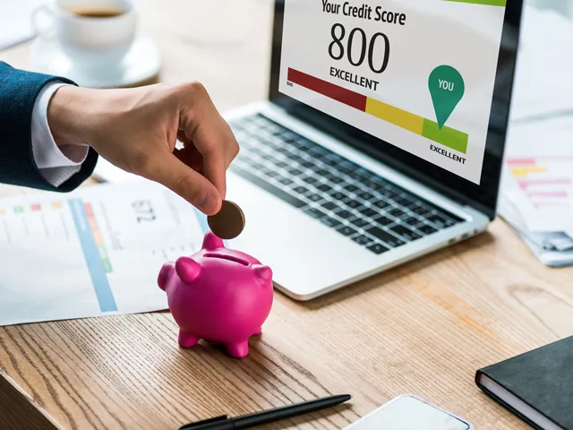 A person putting money into their piggy bank savings while checking out their credit score
