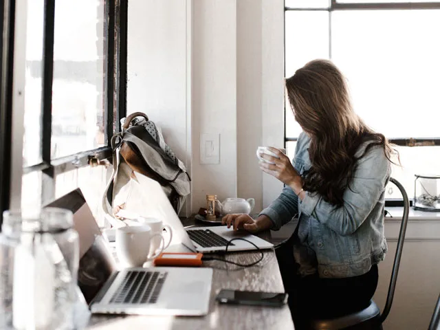 A digital marketing intern doing client work on their laptop while drinking a coffee